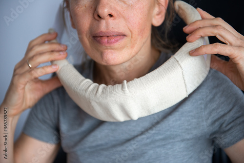 Mature woman in pain wearing a surgical collar on her neck ,working on computer in business office 
