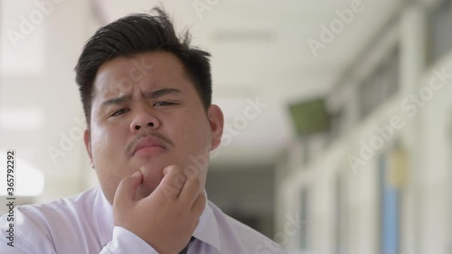 A fat Asian man wearing an office suit and wearing a necktie and a white shirt, looks confused, frustrated, and misunderstood.