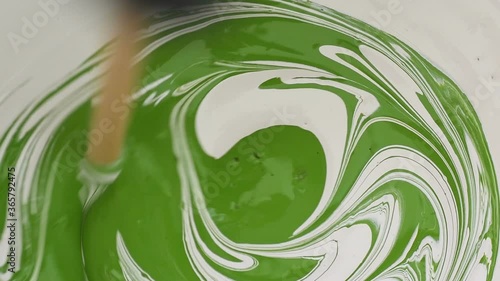 Mixing two colours paint, white and green. Slowly stirring in spirals, adding pigments and toning. Slow motion artistic footage. Art house industrial decor design drawing concept