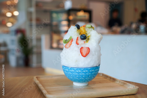 Fruity Kakigori. A bowl of Japanese shaved ice, snow ice flakes topped with strawberry, blueberry, kiwi and passion fruit on wooden plate and table.