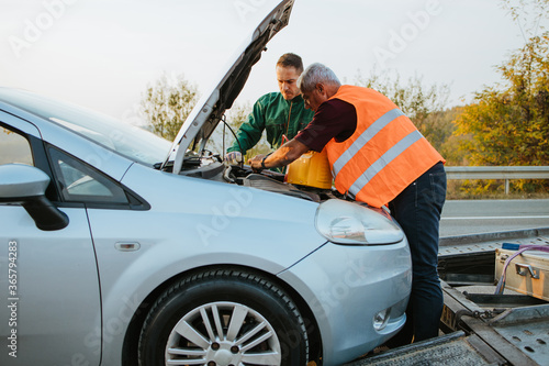 Two road assistant workers in towing service trying to start car engine with jump starter and energy station with air compressor. Roadside assistance concept. © Dusko