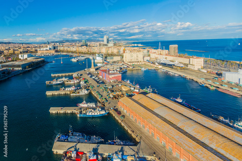 Aerial view of the pier of the port of Barcelona with boats anchored on calm waters on the shore with the horizon and the sea in the background, sunny day with a blue sky and white clouds in Spain