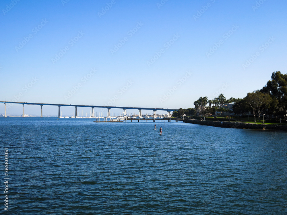 Two friends are enjoying the San Diego bay, where the US navy naval base is located, by rowing in a beautiful day. Coronado bridge is in the background.