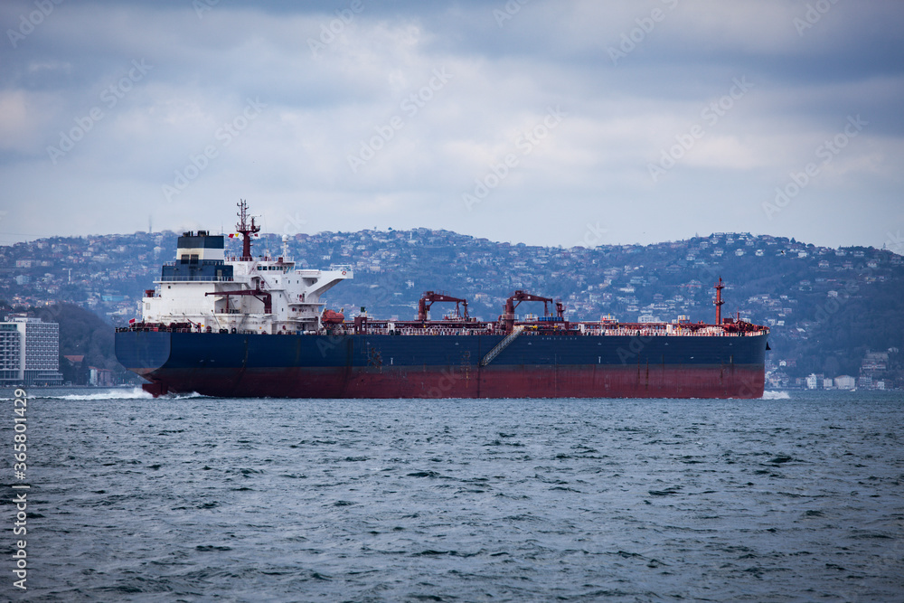Fototapeta premium Huge tanker is passing through Istanbul strait or Bosporus. Giant cargo ship with couple of cranes over is sailing in Marmara sea on a cloudy day.