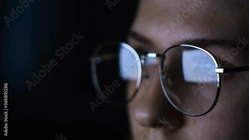 Close-up of woman with glasses looking at computer in dark. Concept. Woman with glasses straining eyes while reading articles on computer in dark