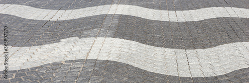 Wavy light and dark gray cobblestone pavement on the street. Panoramic image