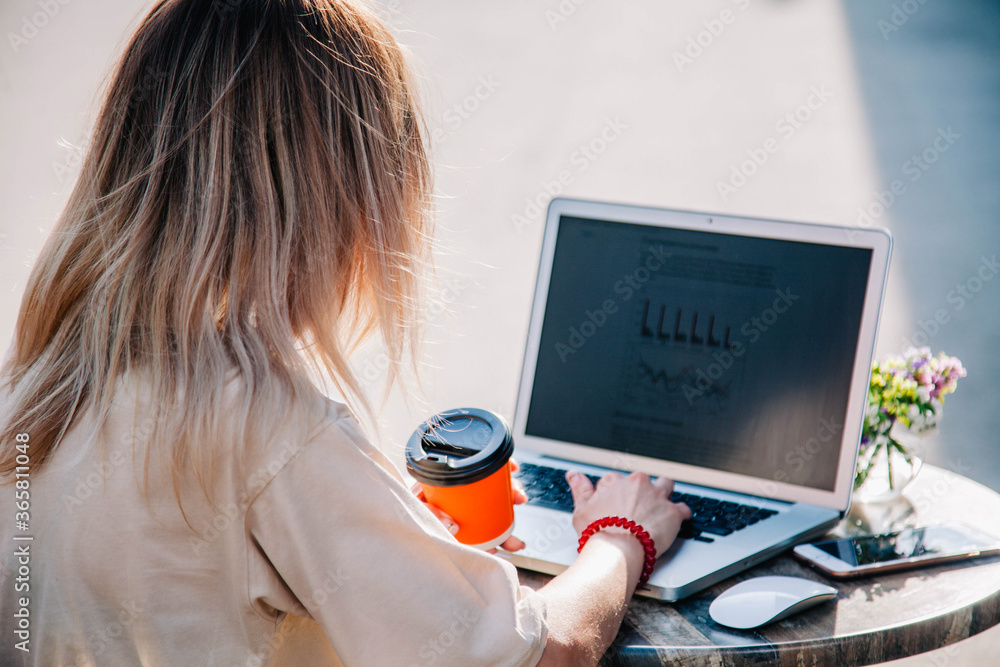 A young girl on a summer playground of a coffee shop works behind a laptop and drinks coffee from a disposable cup A young girl on a summer playground of a coffee shop works behind a laptop and drinks coffee from a disposable cup