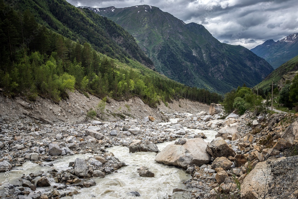 Stony riverbed of Adyl Su river, high green Caucasus mountains on the background. Kabardino-Balkaria, Russia.
