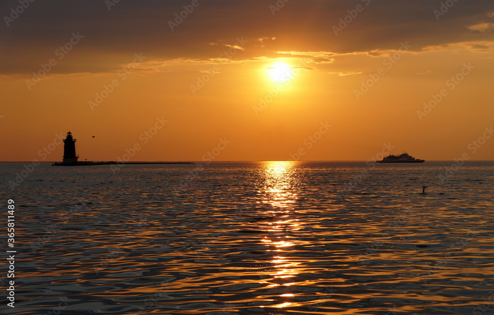 A distance silhouette of the lighthouse and a boat during sunset at Cape Henlopen State Park, Lewes, Delaware, U.S.A