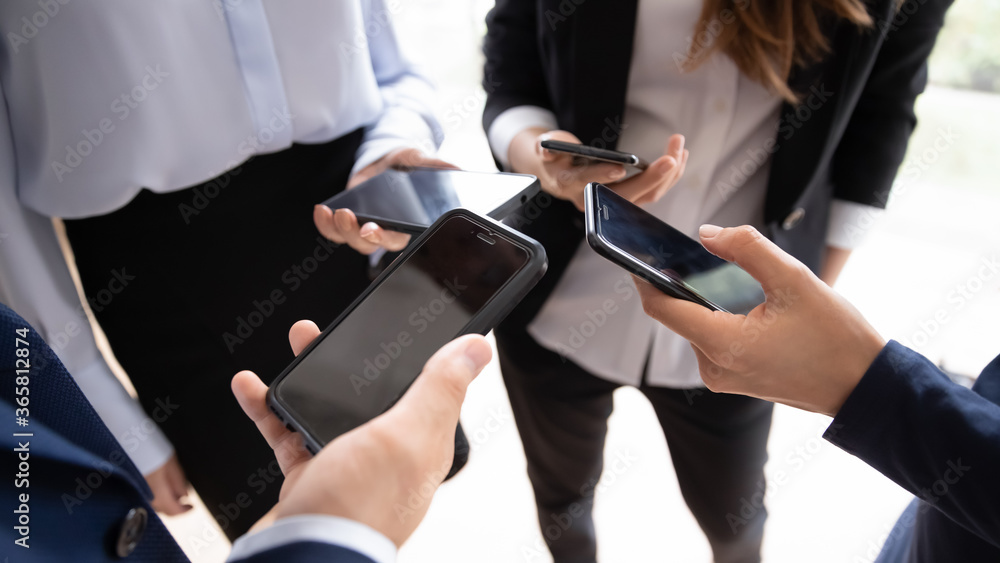 Four entrepreneurs standing in circle close up view on hands holding smart phones. Solving business issues distantly, corporate chat app, business application usage, phubbing, devices overuse concept