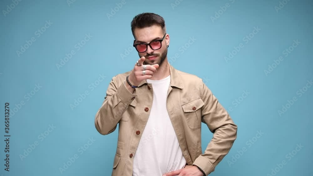 young casual man in jacket making silence, pointing finger and threatening, winking and smiling, pointing finger, making come with me gesture and leaving on blue background young casual man in jacket making silence, pointing finger and threatening, winking and smiling, pointing finger, making come with me gesture and leaving on blue background