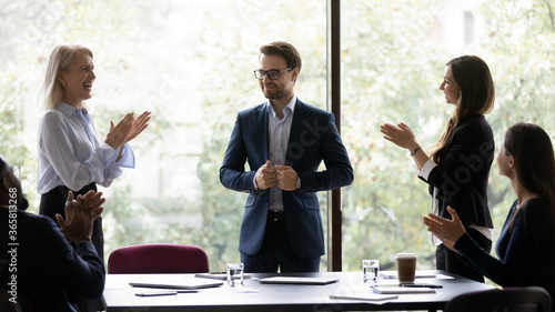 Group of diverse colleagues congratulating applauding and cheering happy businessman with business achievements, career advance, great work results, job promotion standing in modern office board room photo