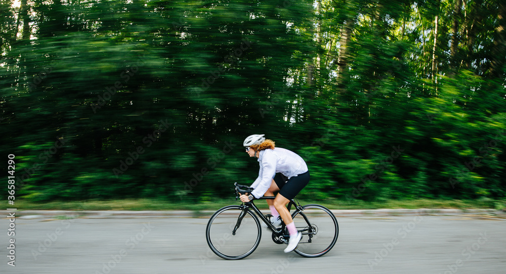 Fototapeta premium Side view of young athletic woman cycling on professional bike in a white helmet