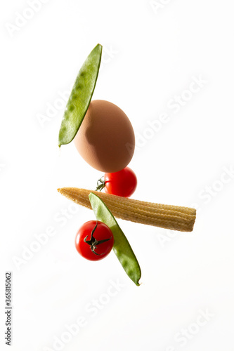 composition of flying vegetables and ingredients beans tomatoes an egg and corn on white background