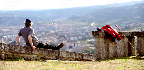 Senior man with backpack and hiking stick looks at a city from a hill photo