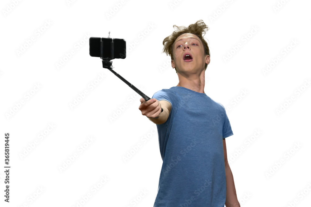 Teen boy is holding selfie stick with smartphone and posing. Isolated on white background. Teen boy is holding selfie stick with smartphone and posing. Isolated on white background.