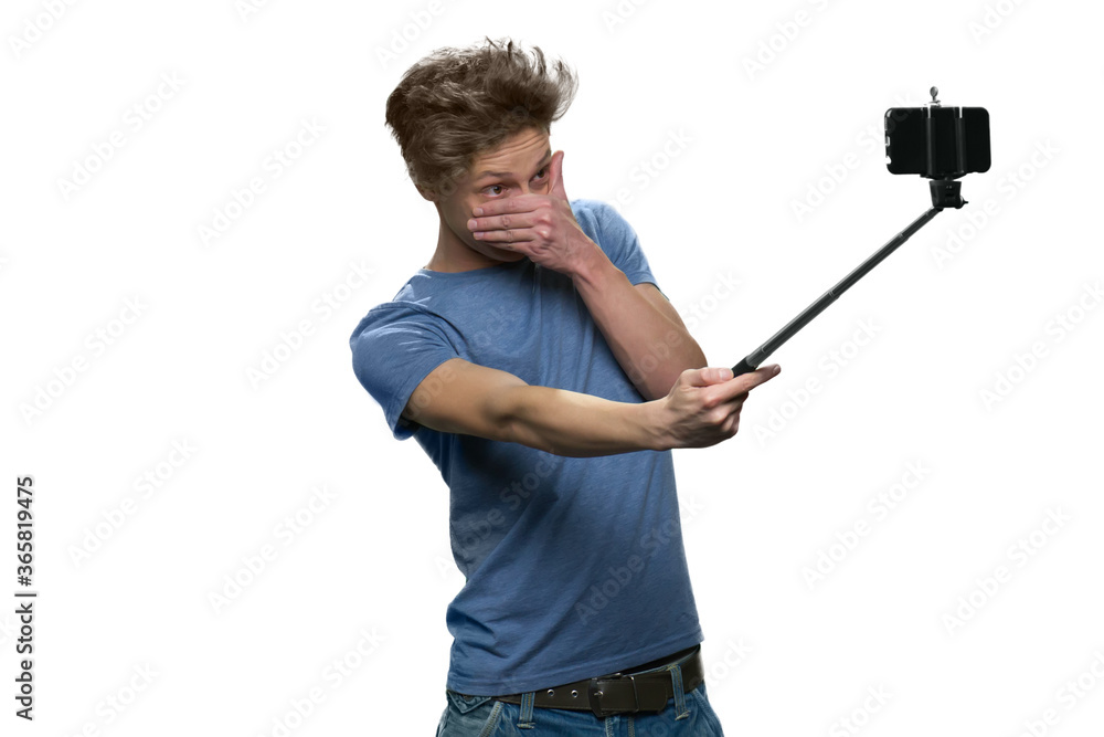 Teenage boy is making selfie and covering his face. Holding selfie stick with smartphone isolated on white. Teenage boy is making selfie and covering his face. Holding selfie stick with smartphone isolated on white.