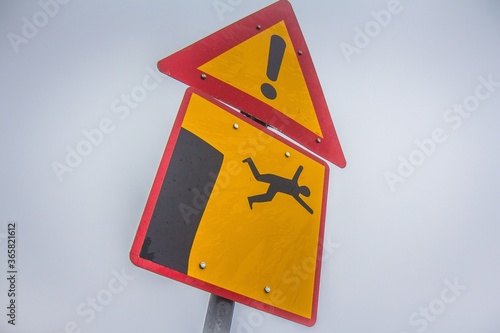 Yellow sign warning about high and dangerous cliff. Man falls from cliff icon. photo