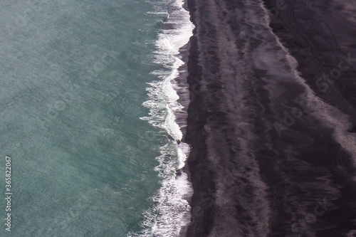 Foamy waves are rolling on the beach with black volcanic sand. Iceland.