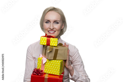 Pretty blonde woman in white blouse holding bunch of gift boxes on white background. Girl looking positively at camera with kind smile.