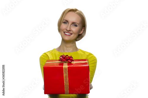 Happy girl gives a gift on white background. Smiling young woman spread his arms forwardly with present. Cheerful young attractive woman.