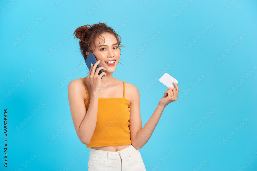 Portrait of pleased woman talking on mobile phone and holding credit card in hand isolated over blue background Portrait of pleased woman talking on mobile phone and holding credit card in hand isolated over blue background