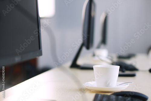 White ceramic cup of hot coffee or tea on wooden computer desk with natural light in the morning at office. Caffeine drinks cause a fresh and aromatic feeling.
