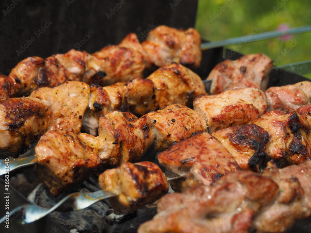 Metal skewers with grilled pork meat on them, on the grill, against the background of green meadow grass.