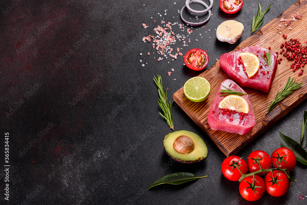 Fresh tuna fillet steaks with spices and herbs on a black background Fresh tuna fillet steaks with spices and herbs on a black background