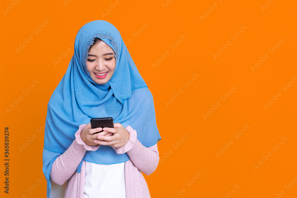 Smiling Asian muslim woman with using mobile or smartphone exciting over isolated color background. Smiling Asian muslim woman with using mobile or smartphone exciting over isolated color background.