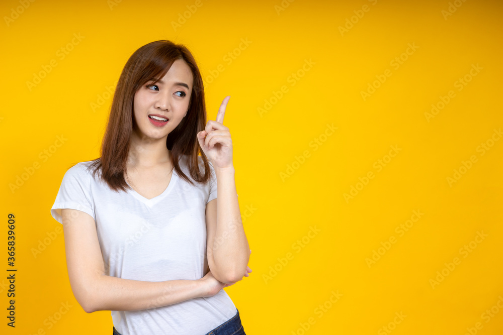 Young elegant Asian woman smiling and pointing to empty copy space isolated on yellow background Young elegant Asian woman smiling and pointing to empty copy space isolated on yellow background