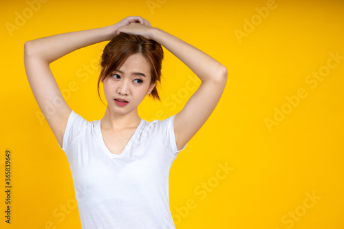 Asian woman gathering her hair over yellow background with copy space