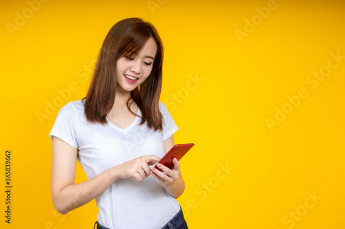 Young elegant Asian woman smiling and using chat or emailing on smartphone isolated on yellow background