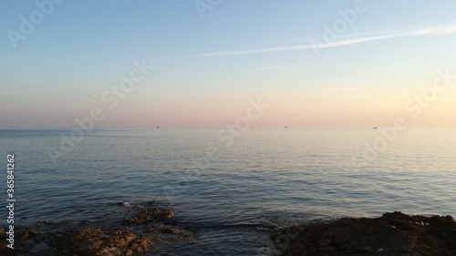 Beautiful sunset by the beach | seaside landscape | dreamy sunrise with creamy pastel colors and calm sea water | beach rocks in front | coast horizontal photography | ocean horizon | coastal scene 