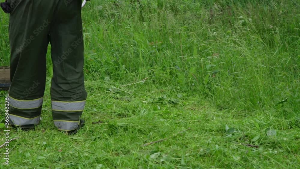 gardener in special jumpsuit cuts green grass with electric lawn mower in local garden n summer day slow motion gardener in special jumpsuit cuts green grass with electric lawn mower in local garden n summer day slow motion