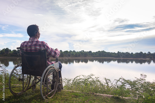 Young disabled man with river background.He is sitting on wheelchair and looking into river.despair,lonely,hope.Photo concept depression and Patient.