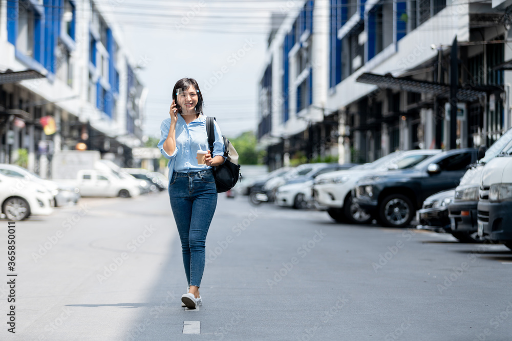Young Asian girl wearing face shield walking in the city with smartphone in her hand Young Asian girl wearing face shield walking in the city with smartphone in her hand