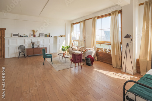 Vintage studio apartment interior in light colors in old style. huge room with large windows with a living room area and a bedroom area. direct sunlight inside.