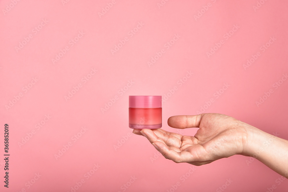 Hand showing pastel pink cosmetic containers packaging over pink background, Facial skincare cream, Blank label for branding mock-up, Beauty product concept.