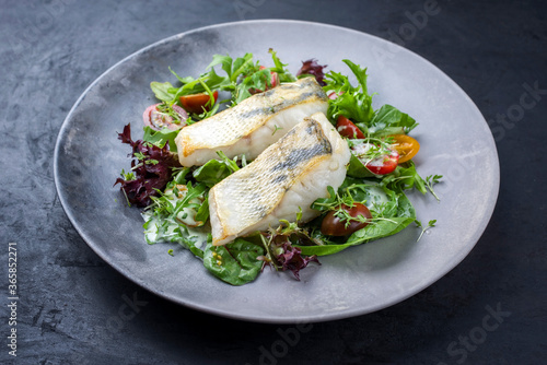 Traditionelles gebratenes Skrei Kabeljau Fish Filet mit italienischen Salat und Tomatenin Zitronen Kokosnus Dressing angeboten als close-up auf einem Modern Design Teller