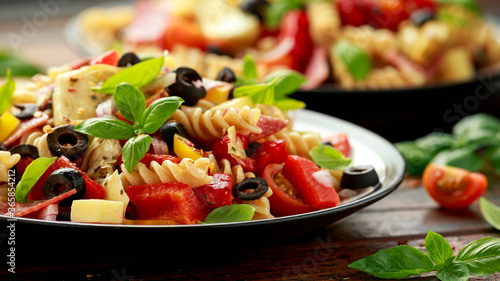 Antipasto salad with pasta  tomato  olives  red onion  bell pepper  salami  cheese  artichoke and basil.