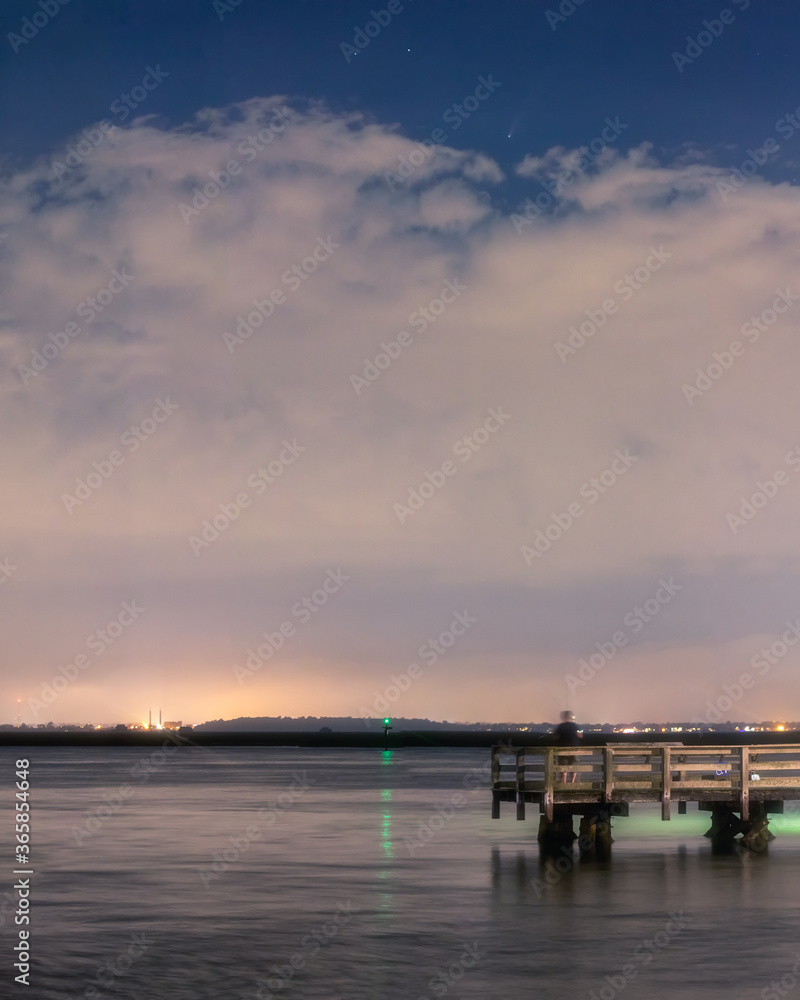 Comet Neowise, setting over a fishing pier and dramatic storm clouds after sunset. Long Island New York