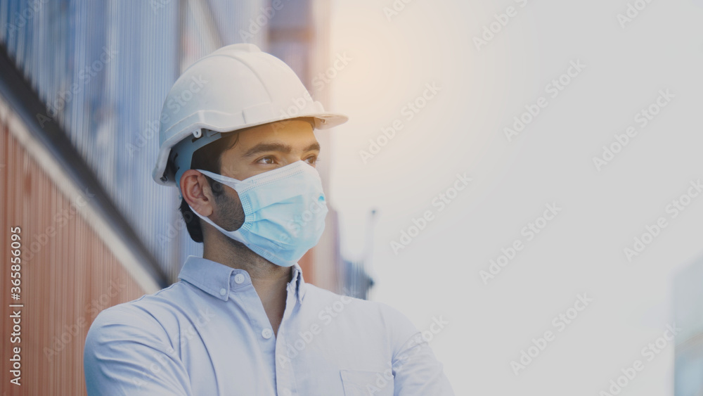 Portrait of a construction worker wearing a hard hat and mask Standing in the workplace Such as container, factory, warehouse For safety during work. Concept Prevent Coronavirus Portrait of a construction worker wearing a hard hat and mask Standing in the workplace Such as container, factory, warehouse For safety during work. Concept Prevent Coronavirus