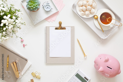 Flat lay desk table. Workspace with modern notebook, stationery, succulent, jewelry and a cup of tea on white table. Top view. Feminine concept