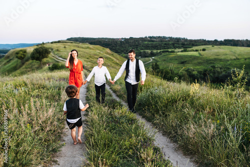 Family of four spend time in the countryside. Happy dad, mom and two sons walk on the dirt road with a scenic landscape on the background