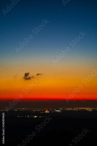 Beautiful landscape colorful dramatic sunset over the mountains valley with orange and blue colors in the clear sky with only one small cloud and lights from buildings in the horizon