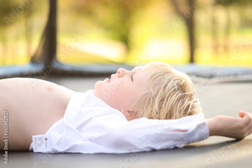 Blonde hair blue eyed boy lying on trampoline with white shirt undone photo