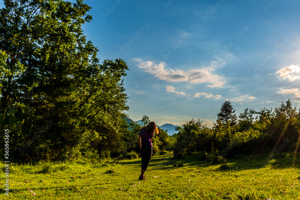 A full body shot of an unrecognizable young Caucasian redhead woman walking in a meadow in a forest in the French Alps during sunset A full body shot of an unrecognizable young Caucasian redhead woman walking in a meadow in a forest in the French Alps during sunset