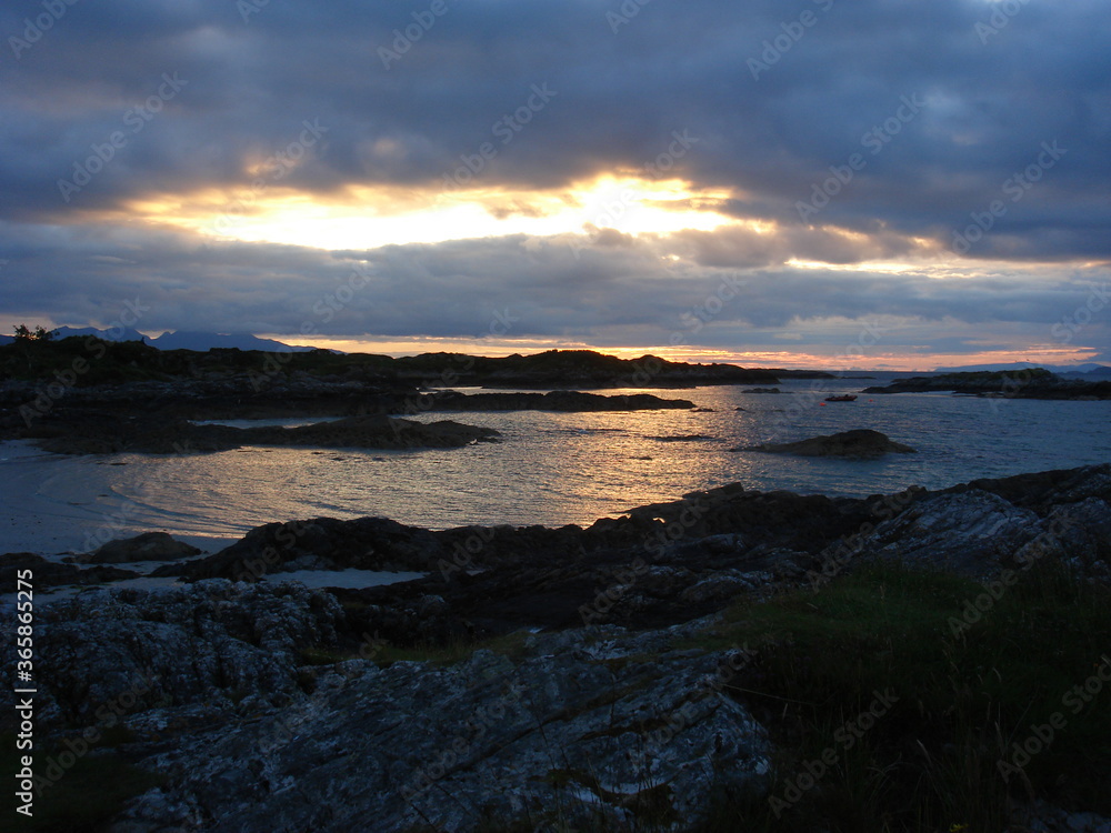 Sunset over the sea off the North West coast of Scotland near Arisaig. Cloudy and rocky islands in silhouette.