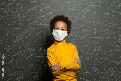 Successful black child boy student in protective face mask on black chalkboard background photo